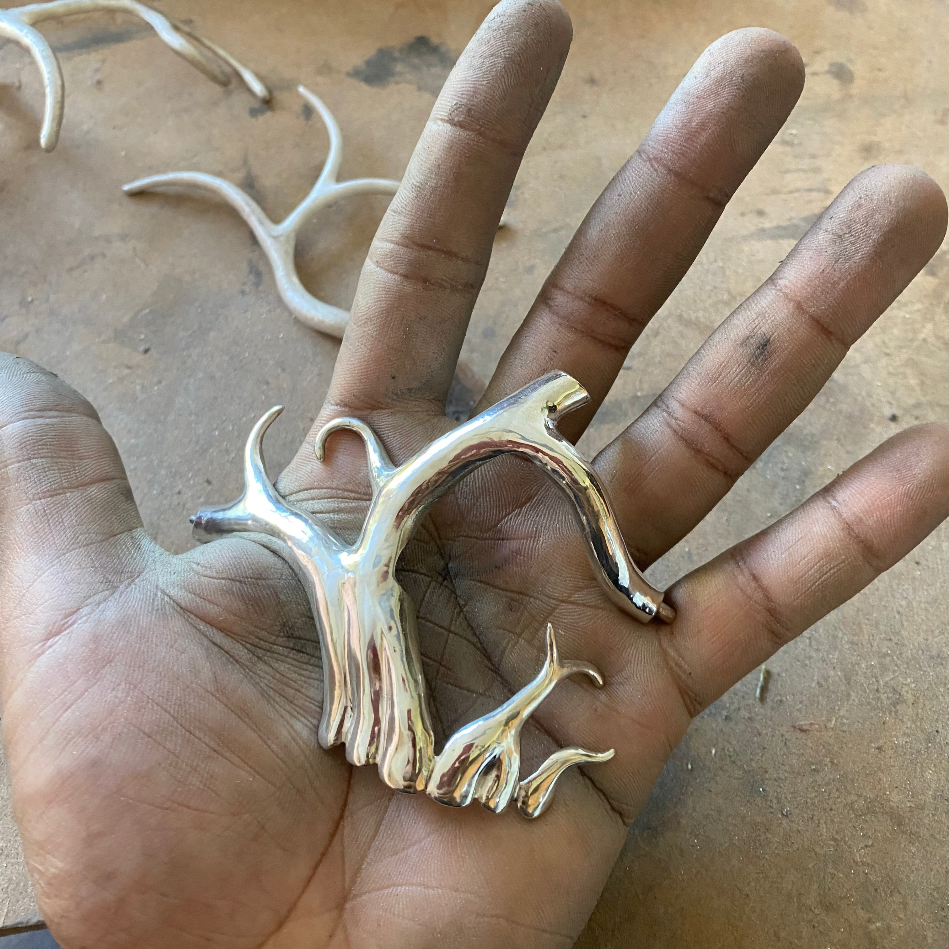 Hand holding a piece of a  silver face mask that resembles a root